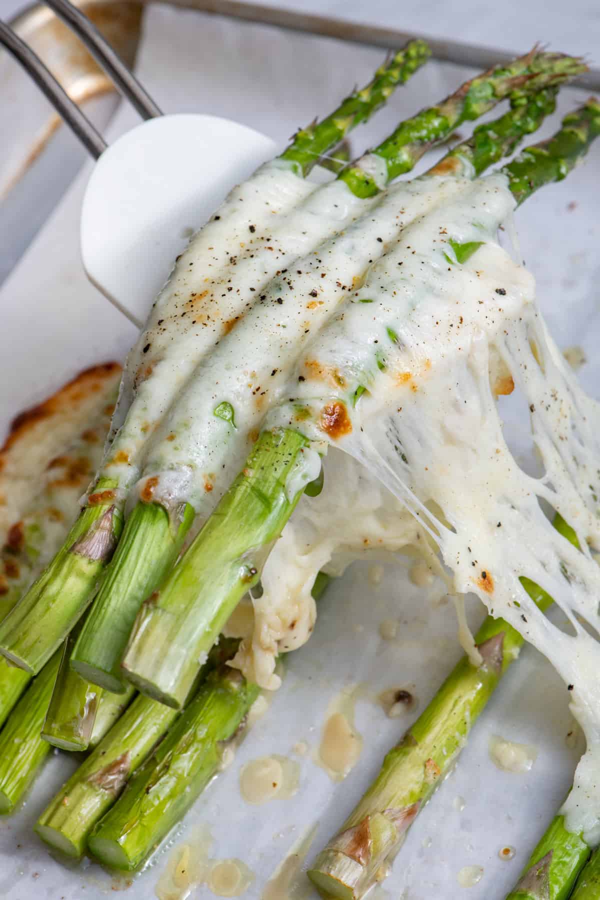 Spatula lifting cheesy oven roasted asparagus