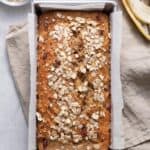 Oatmeal banana bread in loaf pan with oats nearby and banana peel
