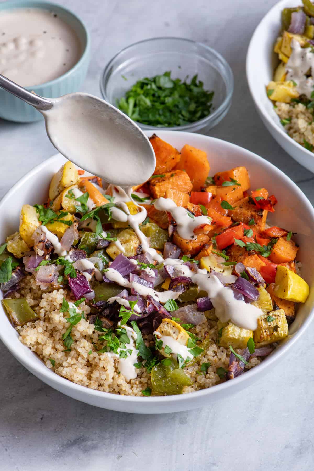 Tahini sauce getting drizzled on top of roasted vegetable quinoa bowl