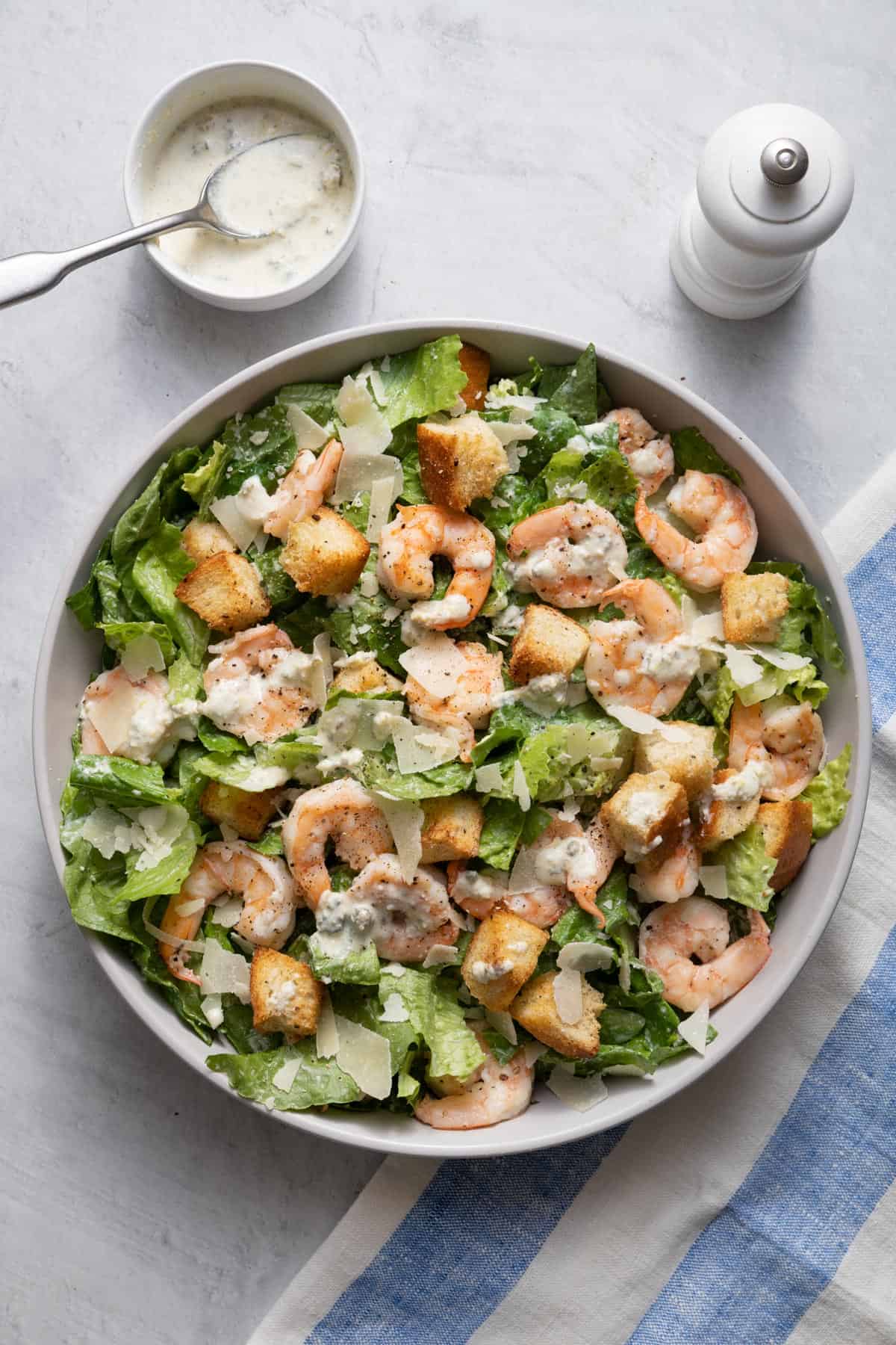 Large bowl of shrimp caesar salad with yogurt dressing on the side