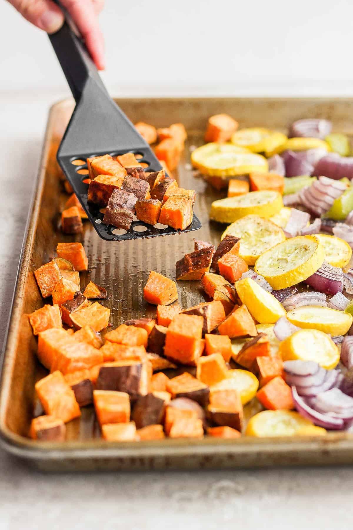 Spatula scraping roasted vegetables from a baking dish