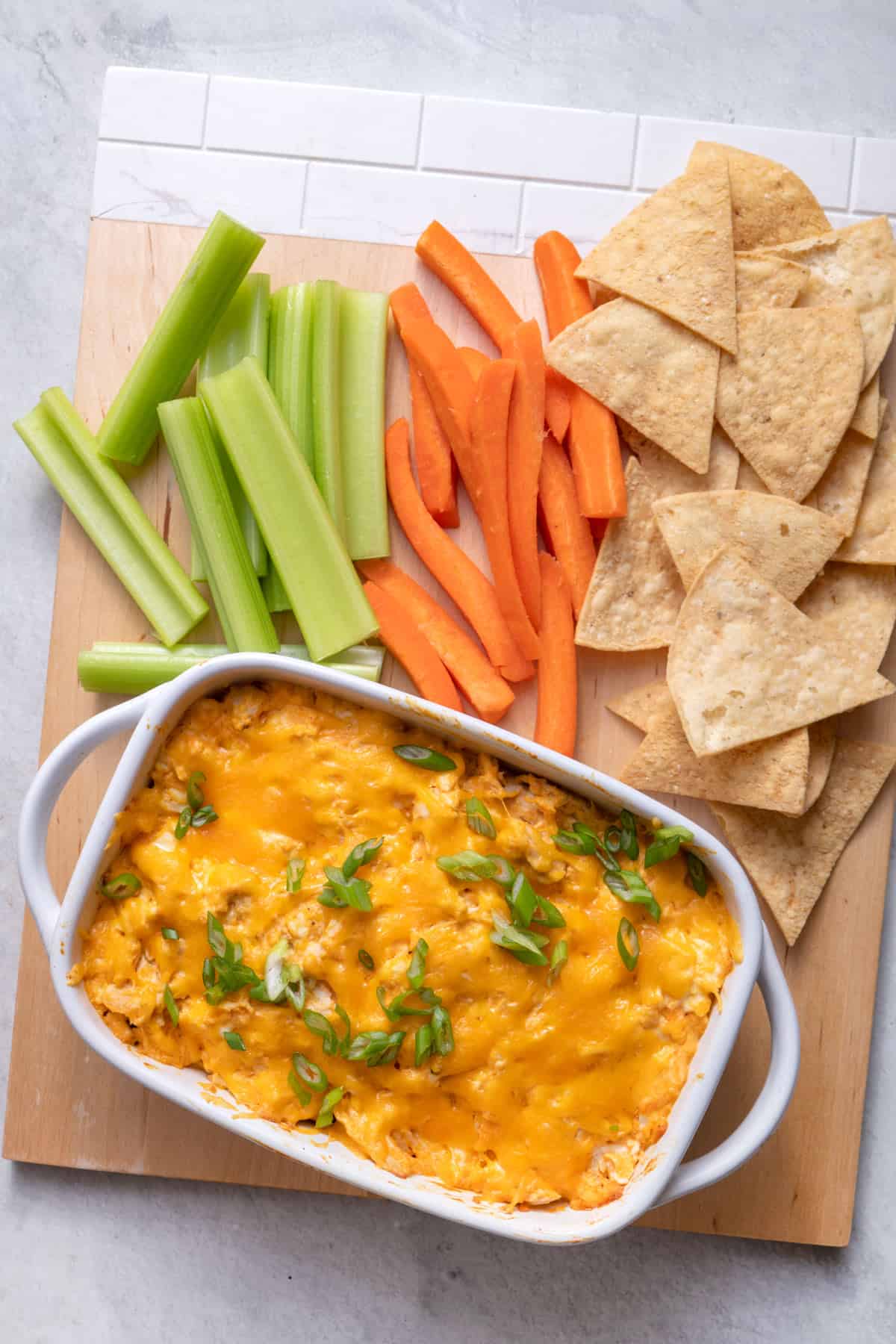 Board with small dish of buffalo chicken dip and veggies and chips