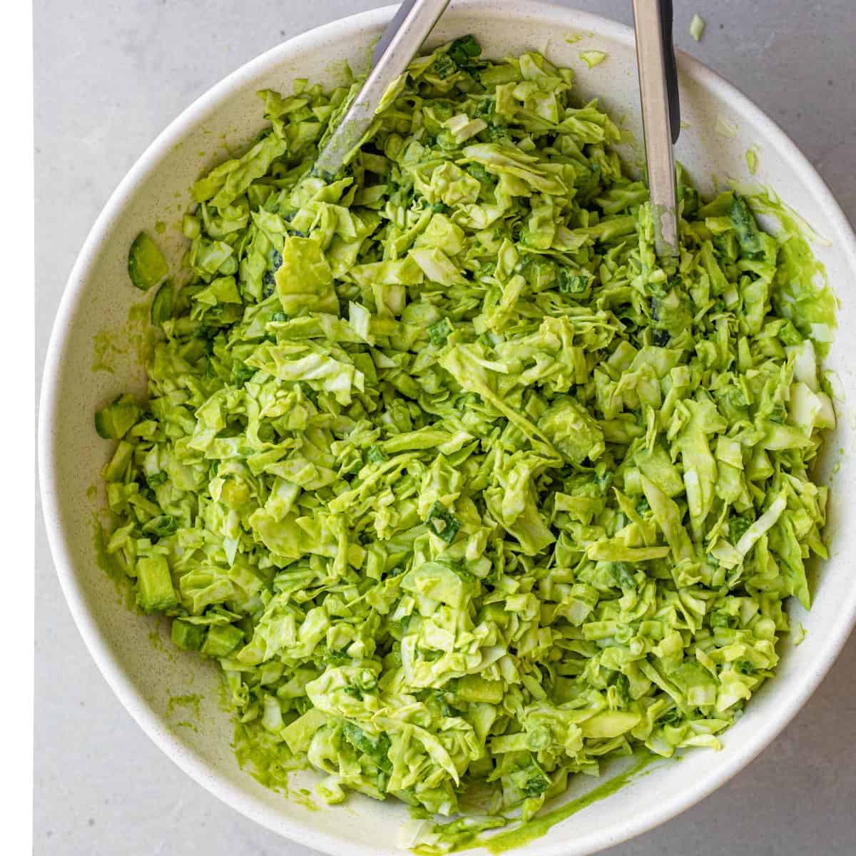 Mixing the green goddess salad together to combine the ingredients with the dressing.
