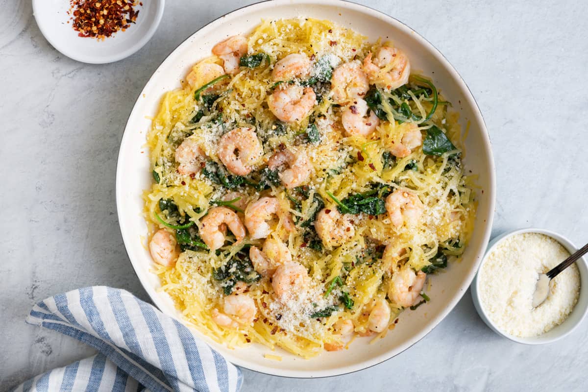 Spaghetti squash shrimp scampi finished product, blue napkin on the side, parmesan cheese and crushed red pepper