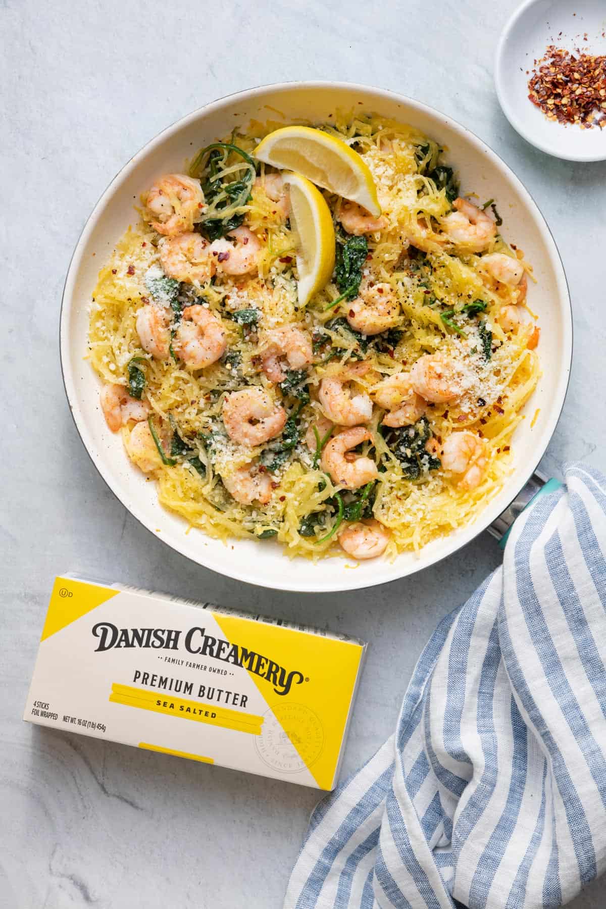 Spaghetti squash shrimp scampi finished product with crushed red pepper in small bowl and package of Danish Creamery on the side