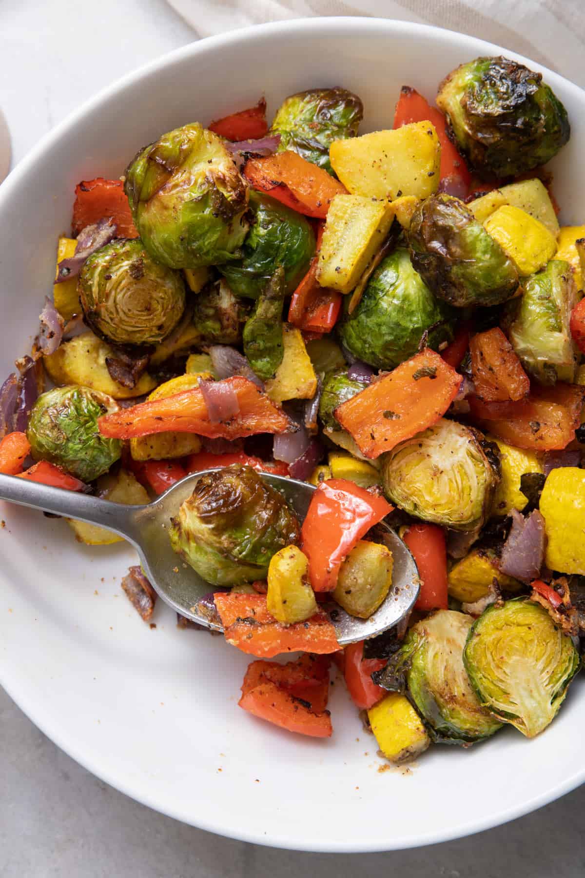 Spoon scooping air fryer vegetables from large white bowl