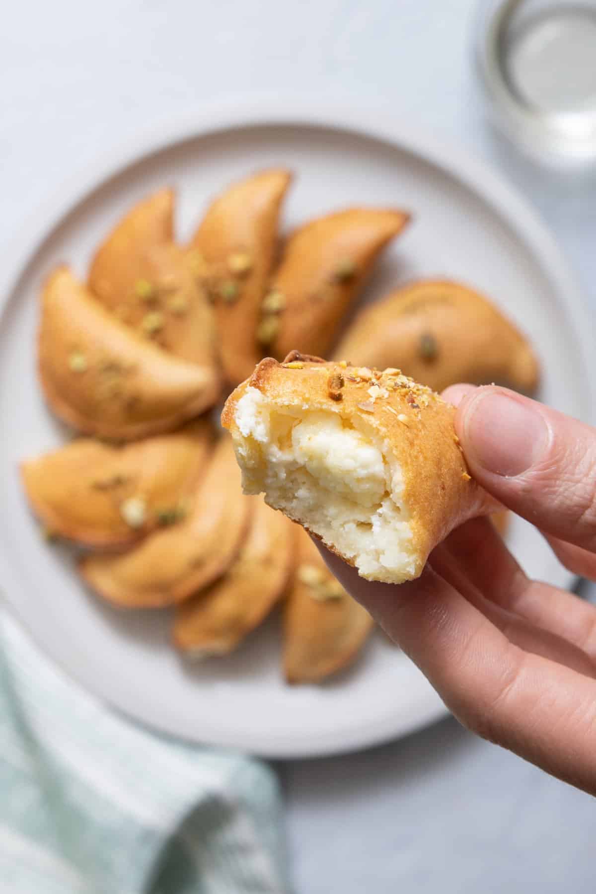 hand holding an atayef with a bite taken out showing cheesy inside