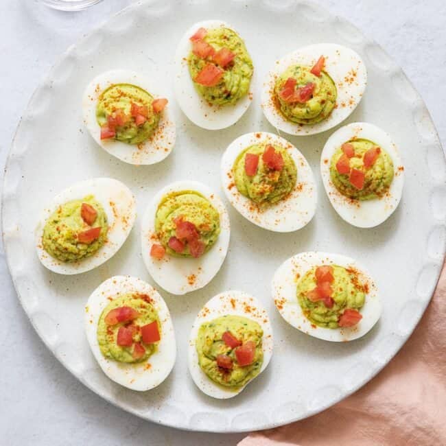 image of avocado deviled eggs topped with diced tomatoes on white wound plate