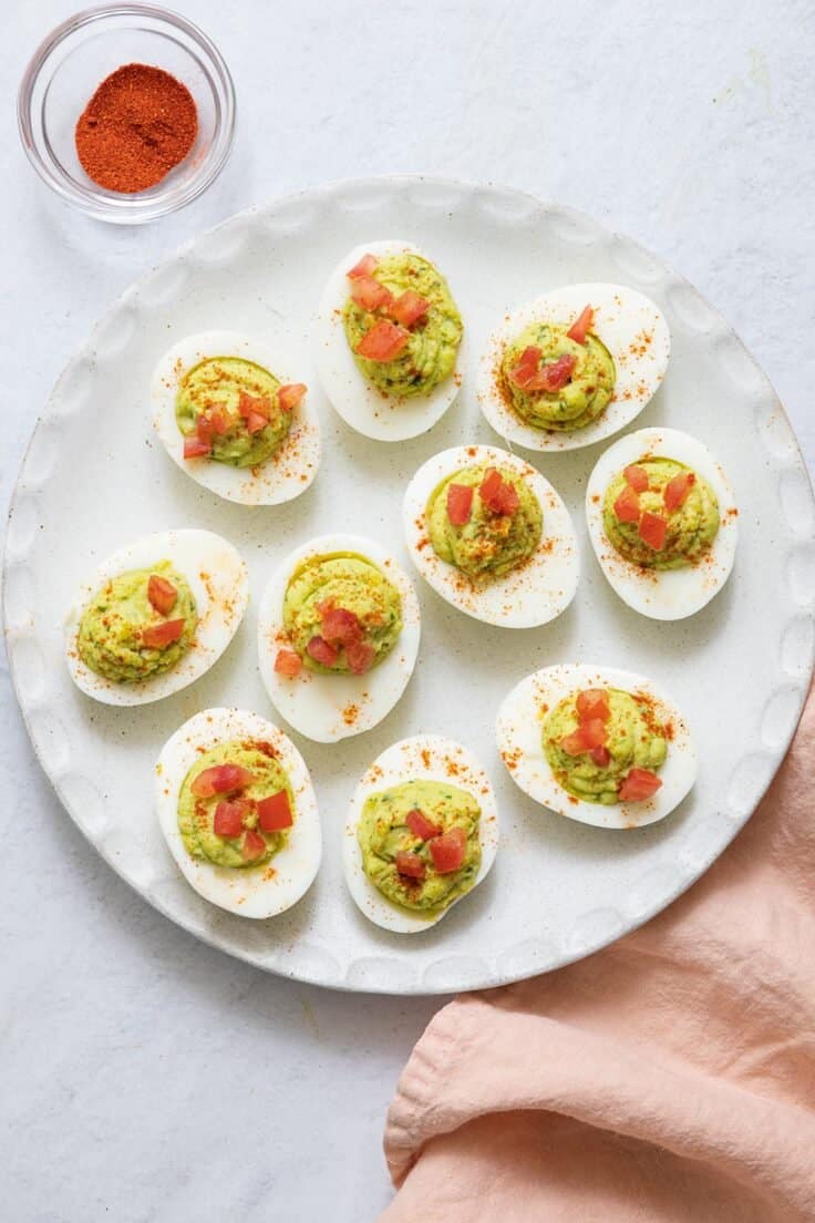image of avocado deviled eggs topped with diced tomatoes on white wound plate