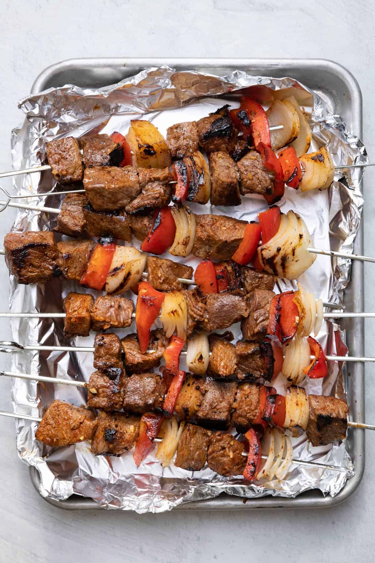 pan lined with foil for metal skewers with cooked ingredients for beef kabobs