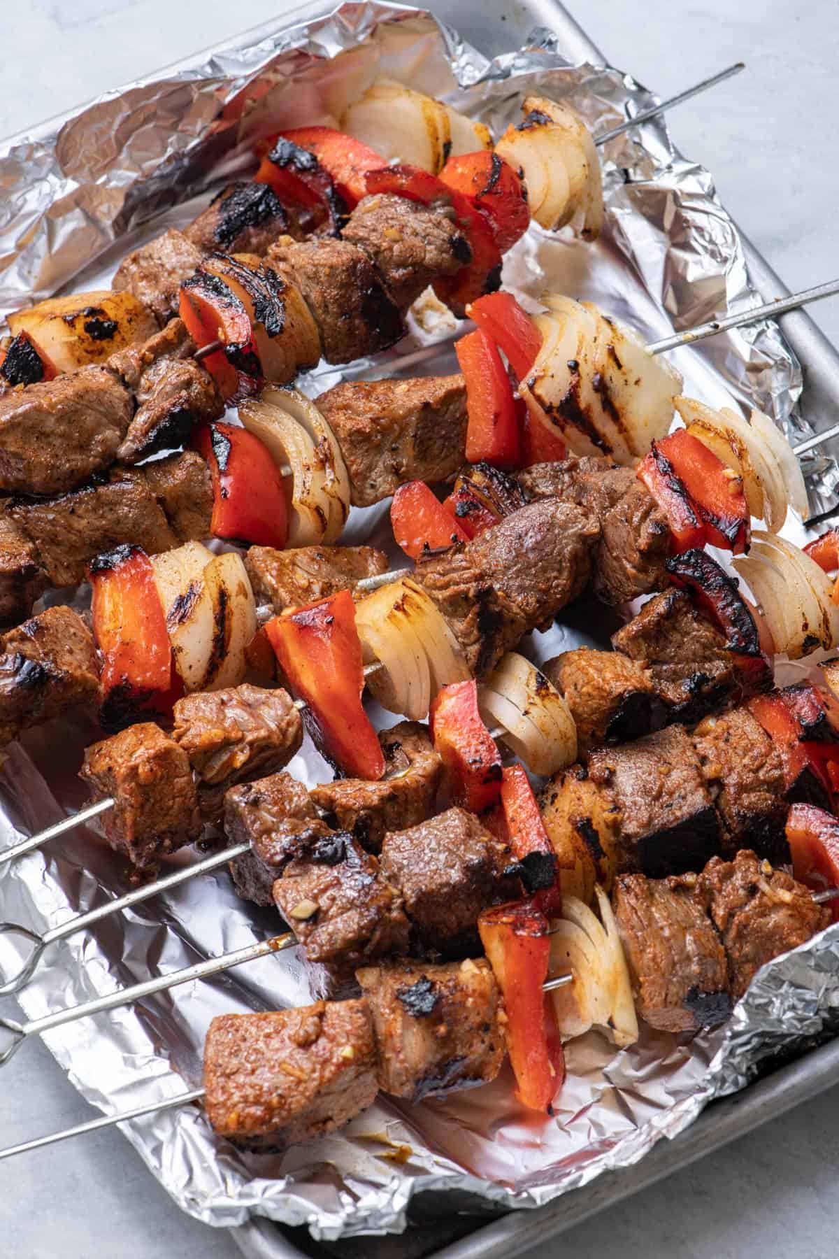 side shot of grilled kabobs on cooking sheet lined with foil