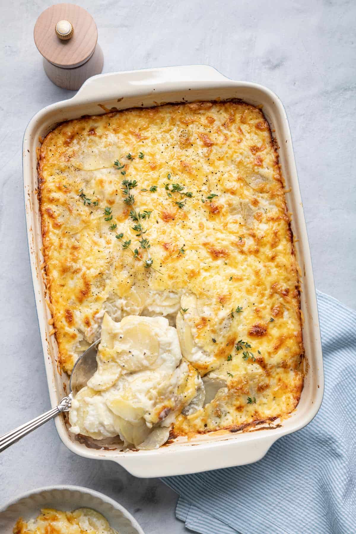 Spoon scooping some of the cheesy scalloped potatoes out of the baking dish