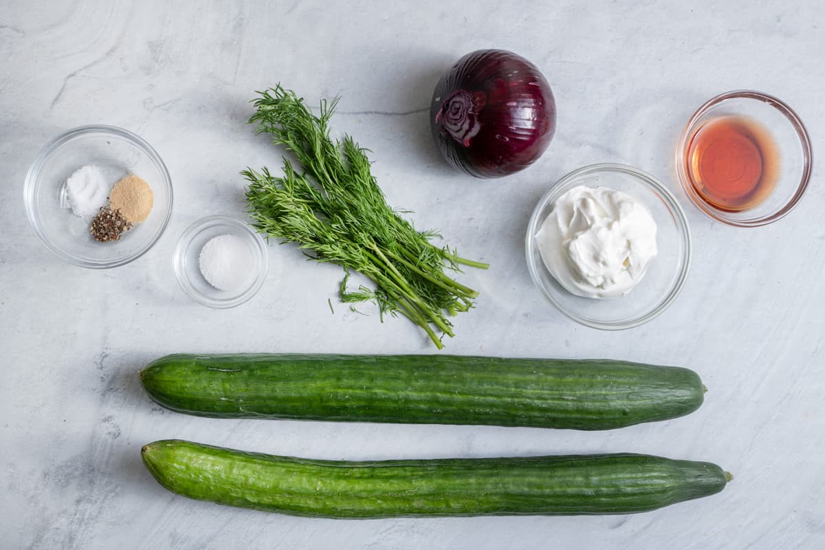 ingredients to make the creamy salad: 2 english cucumbers, seasonings, fresh dill, red onion, sour cream, and red wine vinegar