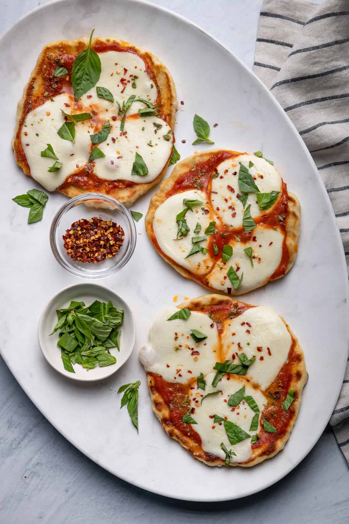 Grilled mini pizzas on serving dish with basil and crushed red pepper