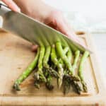 Knife cutting bunch of asparagus on cutting board
