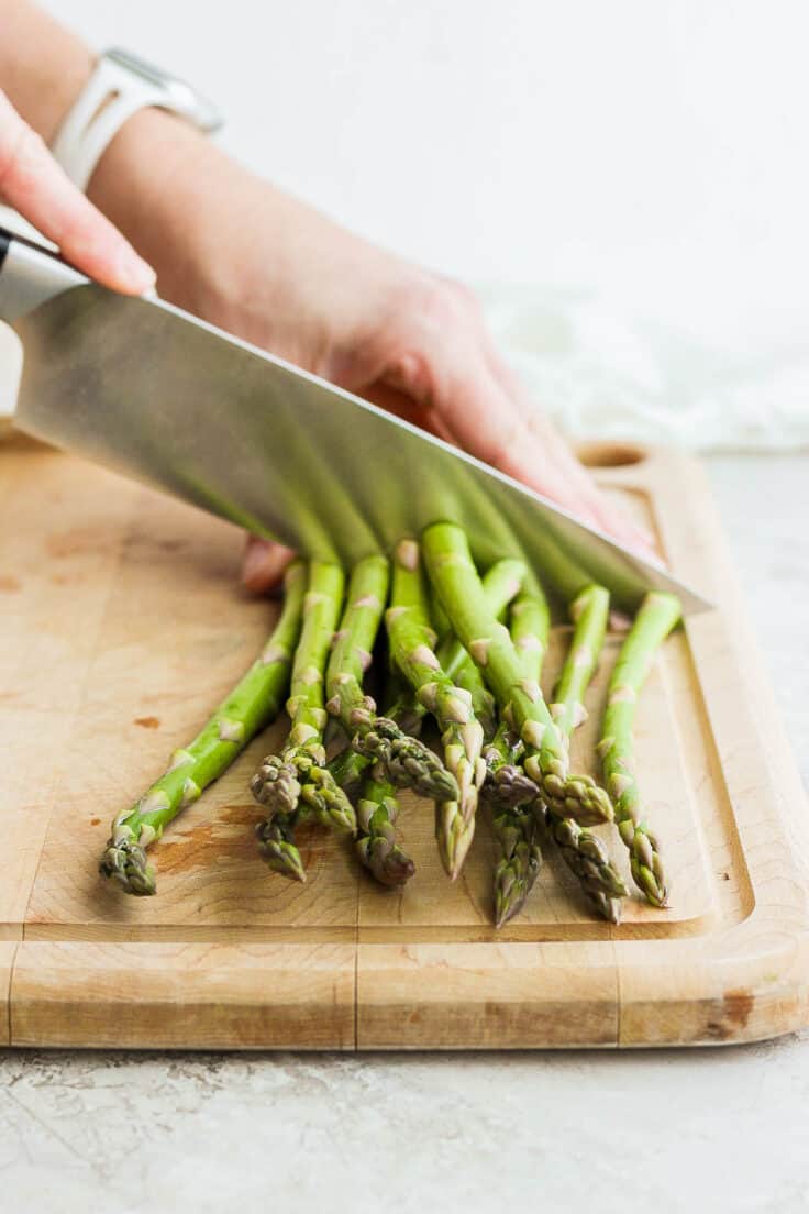 Knife cutting bunch of asparagus on cutting board