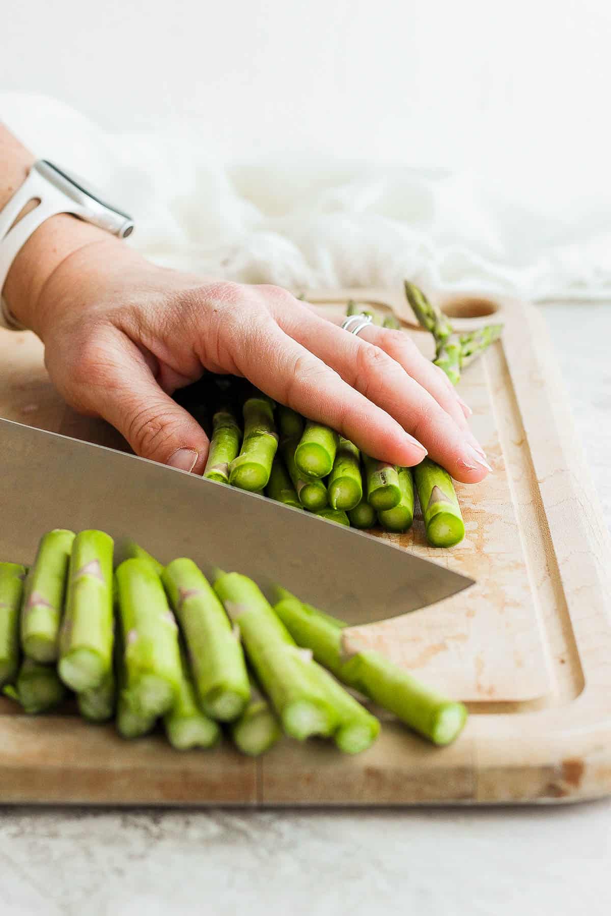 Knife cutting woodsy bottoms off asparagus bunch