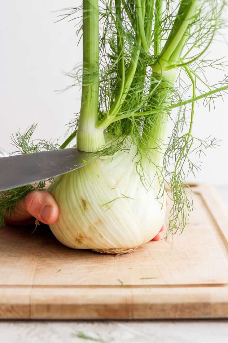 Sharp knife cutting fennel on cutting board