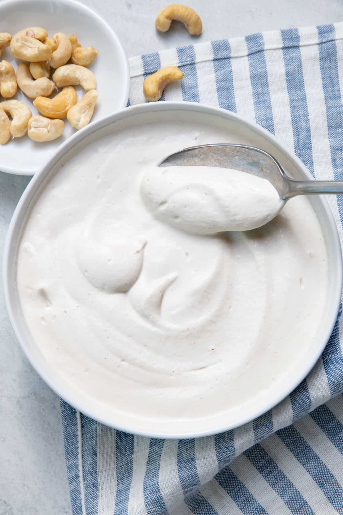 overhead shot of cashew cream in a white bowl with a spoon and small dish with raw cashews to the side