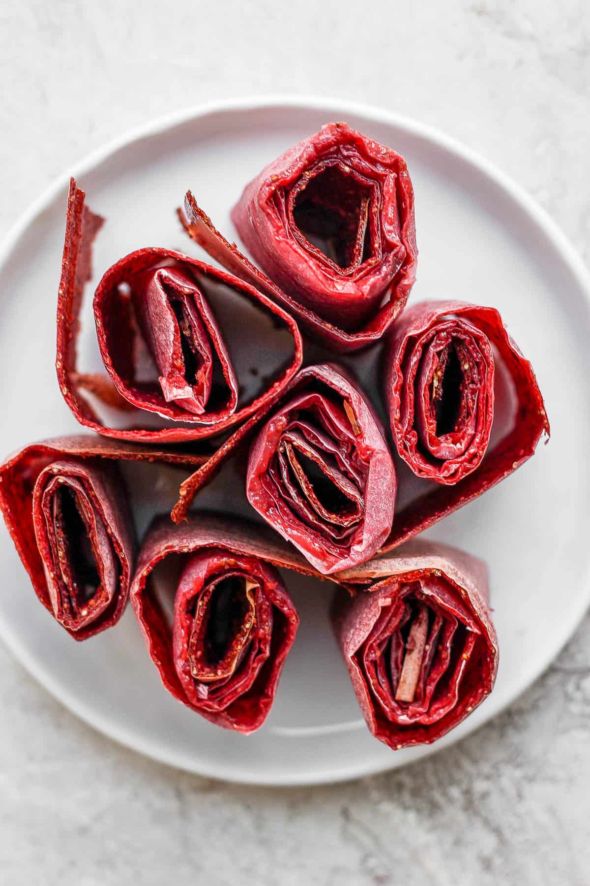 top view of homemade fruit leather rolled with parchment paper on a white plate