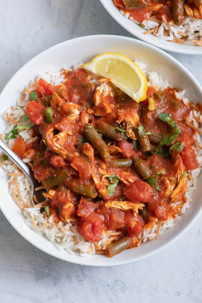 bowl of green bean stew served over Lebanese rice with lemon wedge