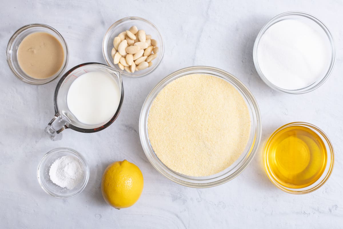 Ingredients for recipe in individual bowls: ghee, milk, baking powder, almonds, lemon, semolina flour, sugar, and tahini