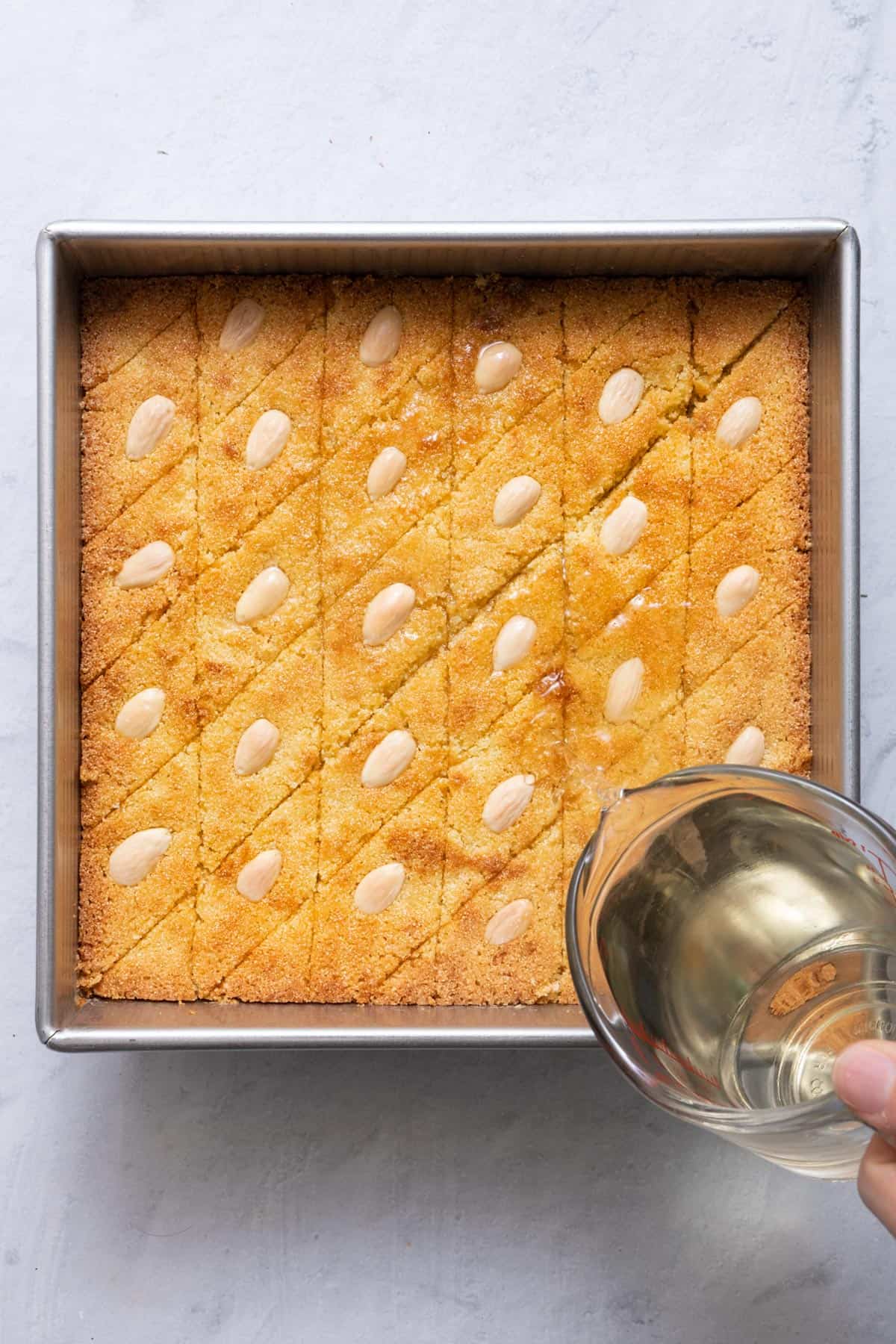 Simple syrup being poured over namoura as soon as it comes out of the oven