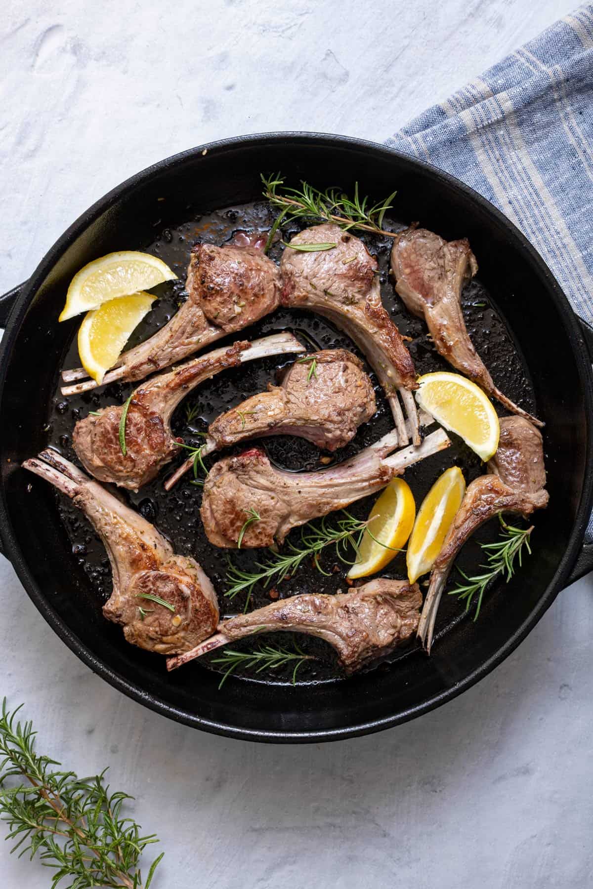 Lamb chops in cast iron skillet garnished with fresh rosemary sprigs and lemon wedges.