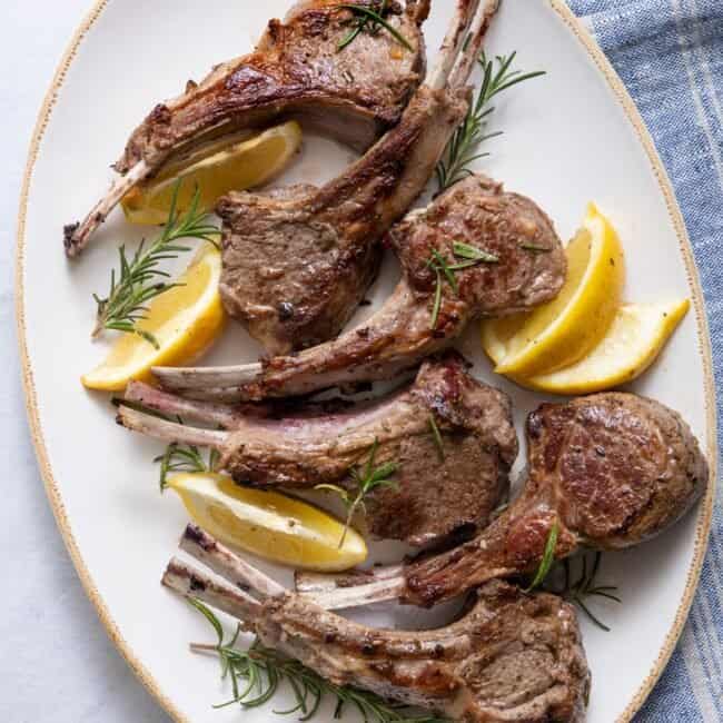 Lamb chops on large serving platter garnished with rosemary and lemon wedges.
