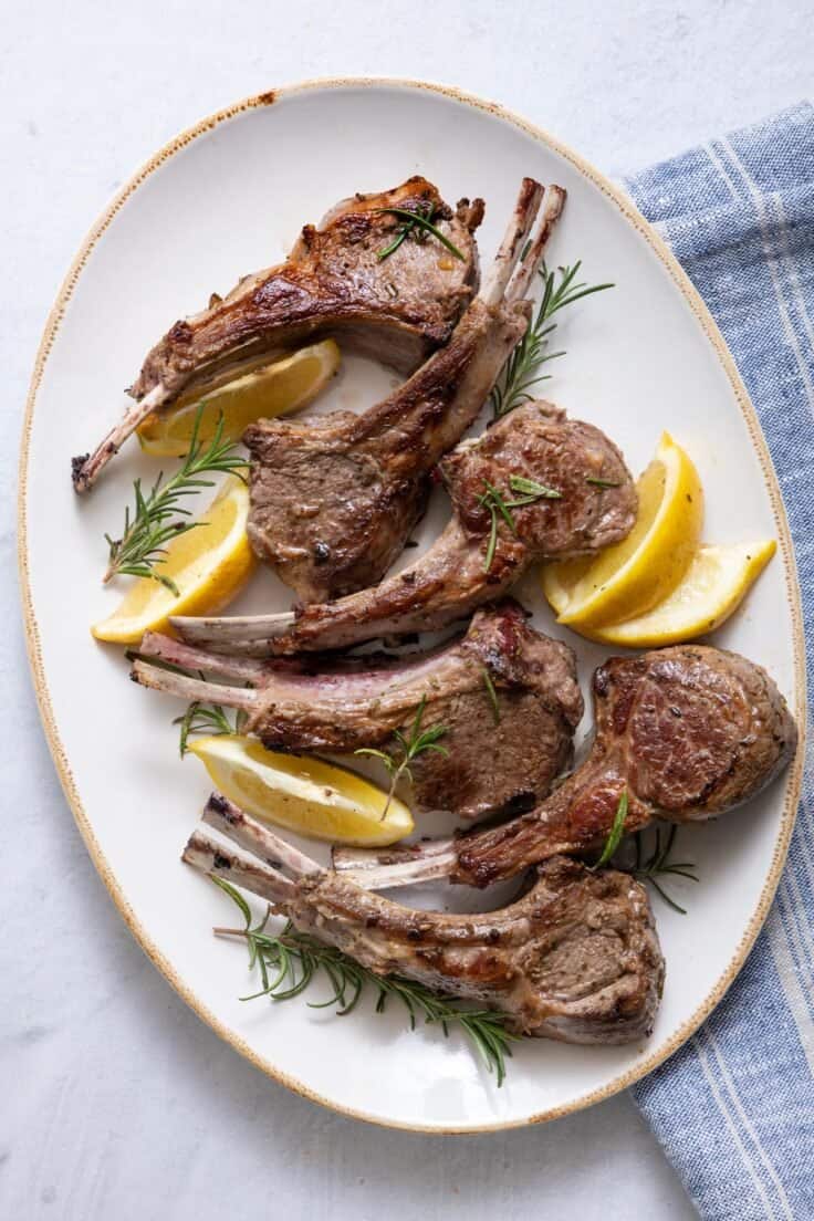 Lamb chops on large serving platter garnished with rosemary and lemon wedges.