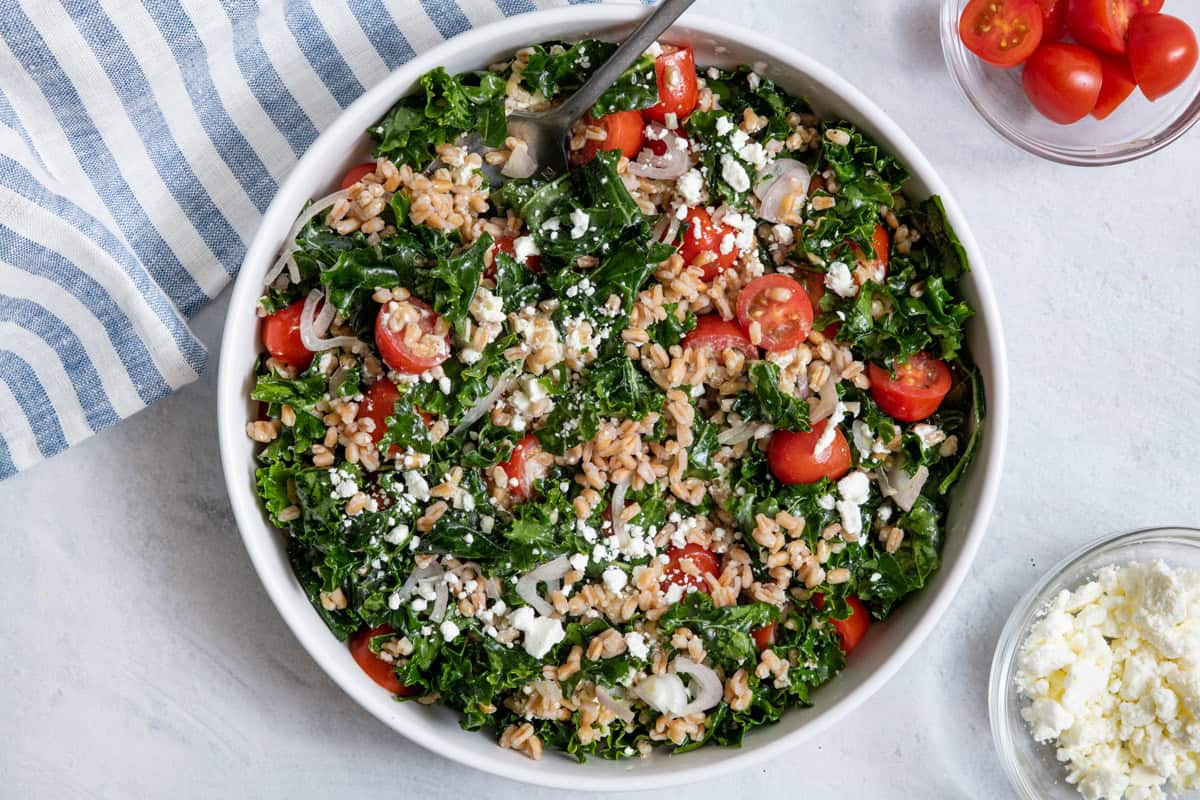 Farro salad served in a large white bowl with a small bowl of goat cheese crumbles.