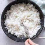 Hand reaching into saucepan with fork and fluffing cooked rice.