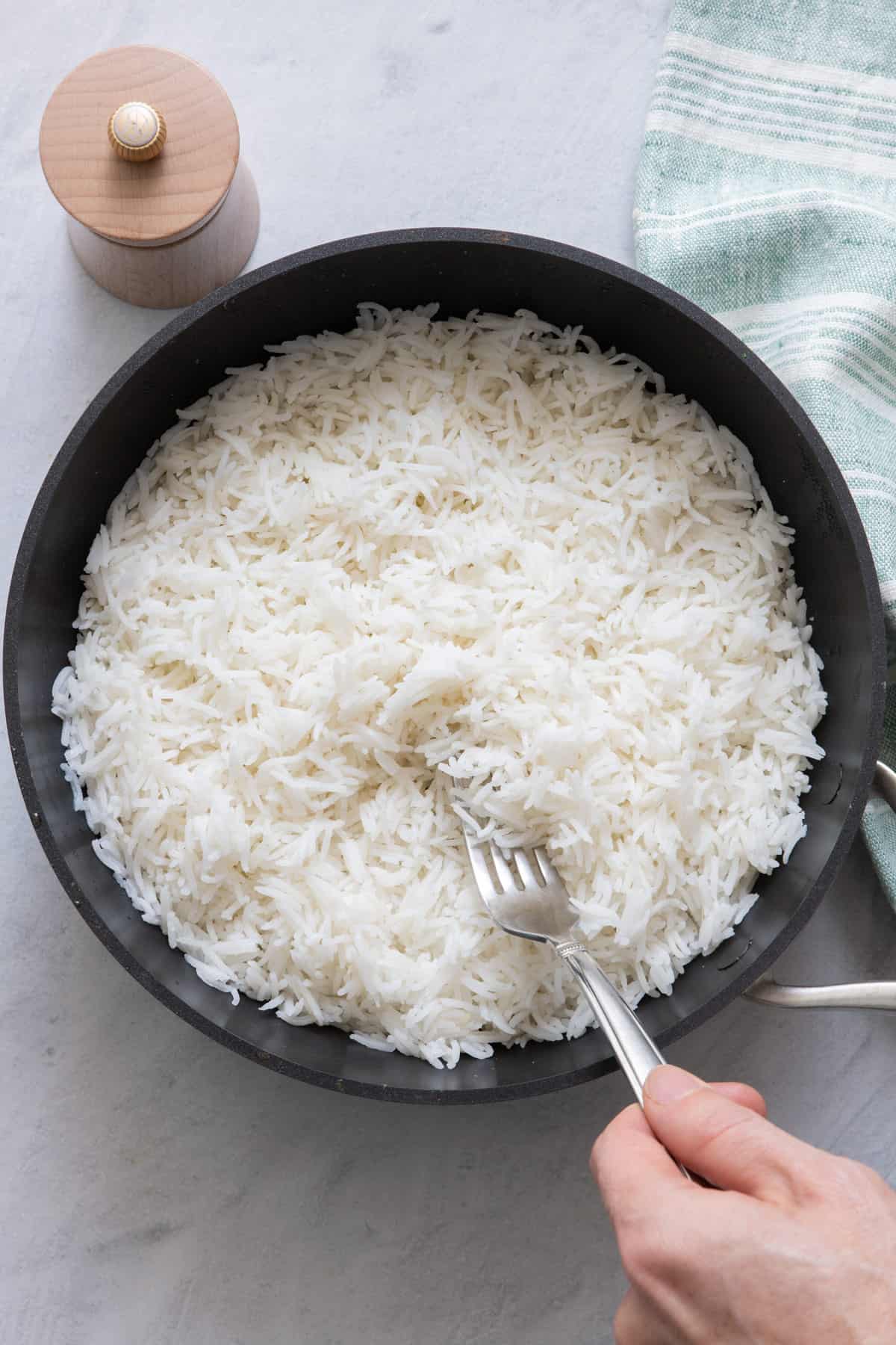 Hand reaching into saucepan with fork and fluffing cooked rice.