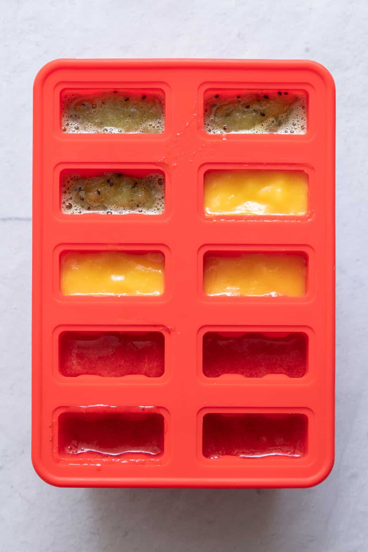 Popsicle freezer tray with 3 different flavors poured inside.