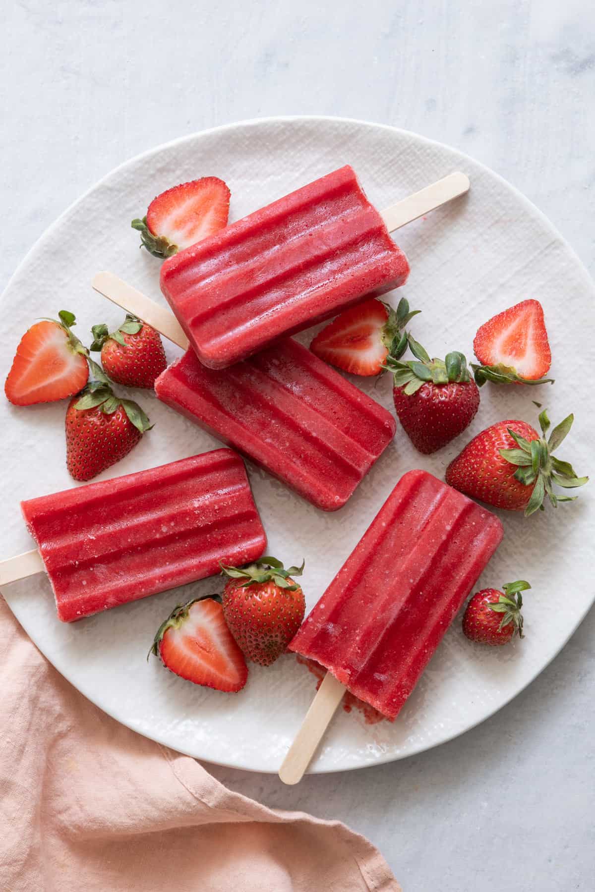 Large plate with four homemade strawberry popsicles and halved fresh strawberries.