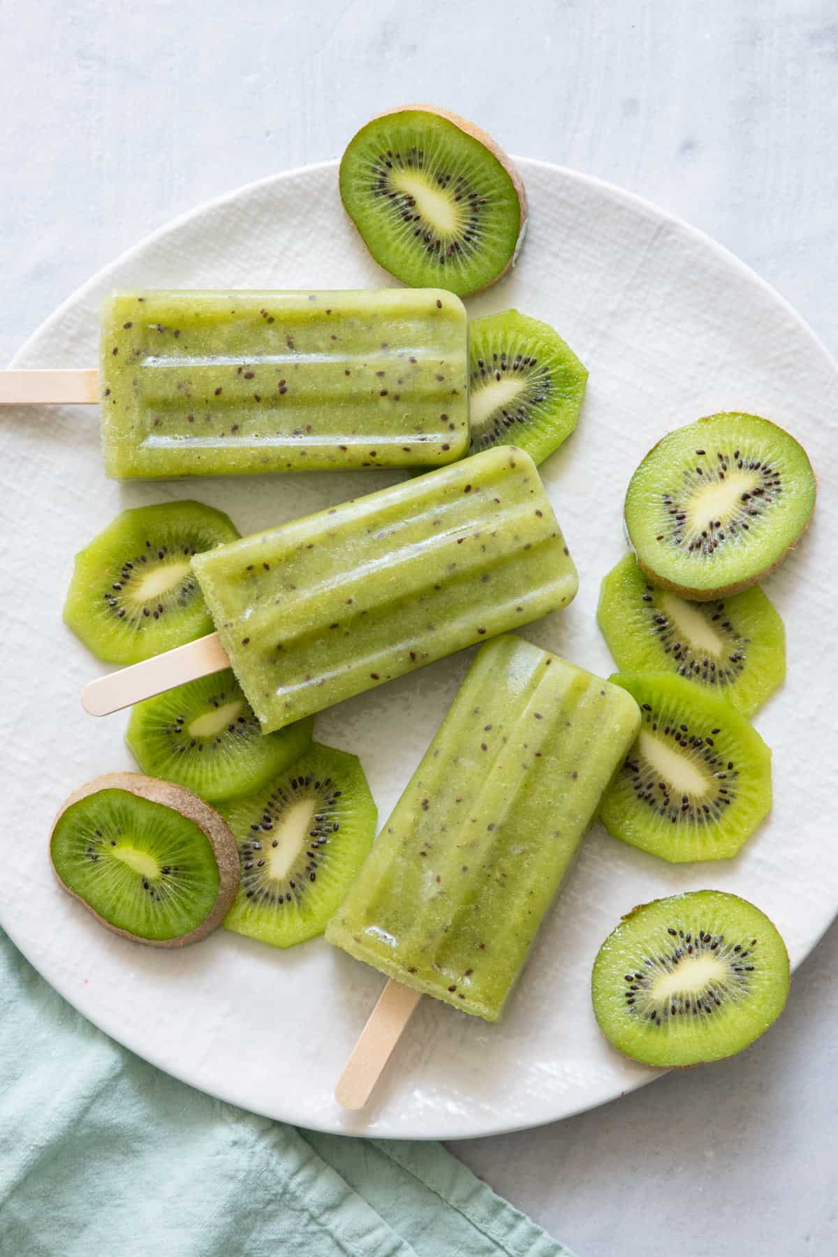 3 kiwi popsicles on plate with slices of fresh cut kiwi.