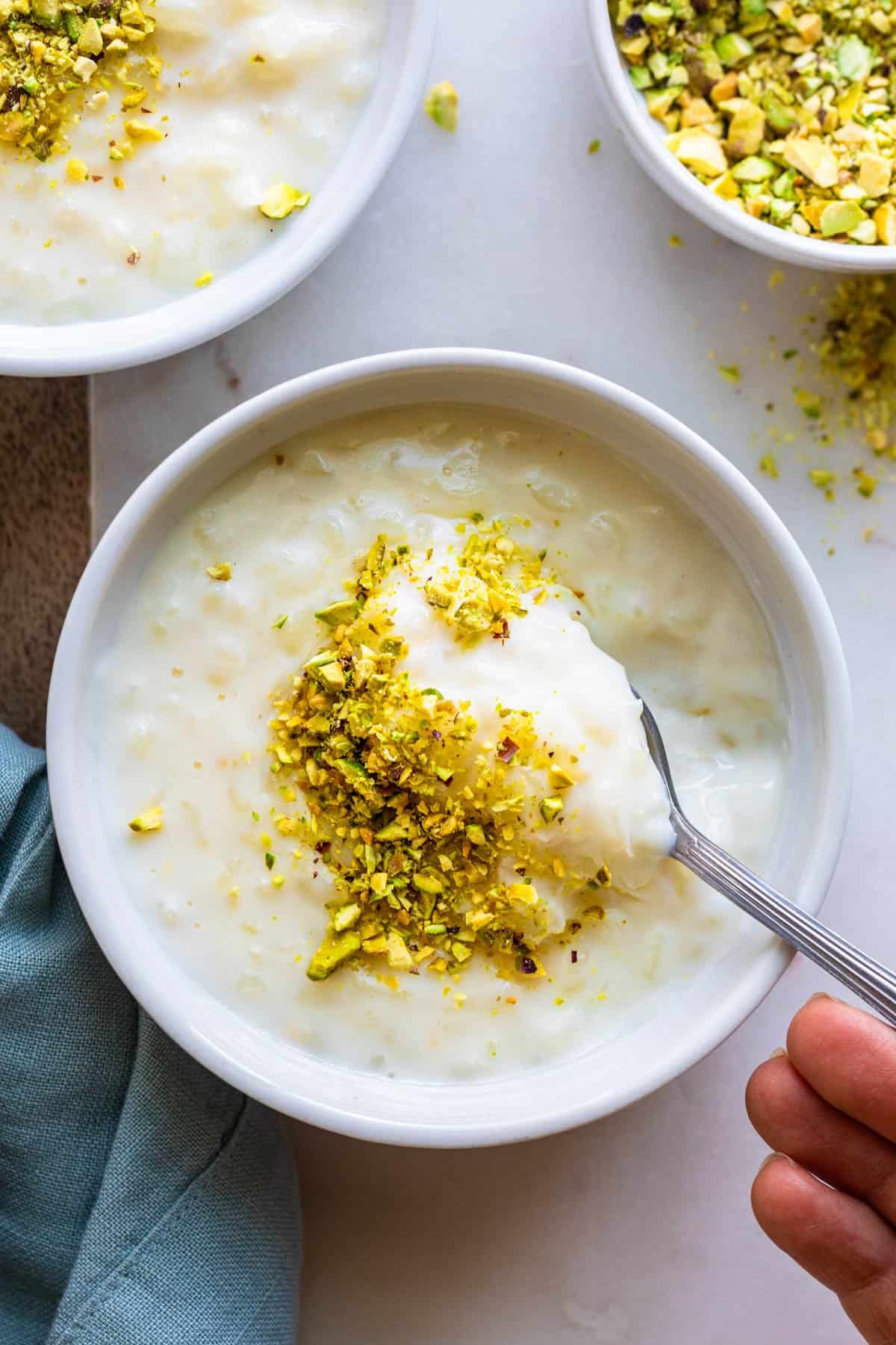 Spoon scooping up rice pudding topped with crushed pistachios.