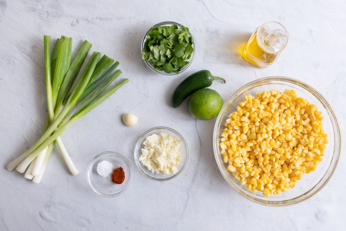 Ingredients for recipe before prepped: corn kernels, avocado oil, scallions, cilantro, cotija cheese, jalapeno, lime, and spices.