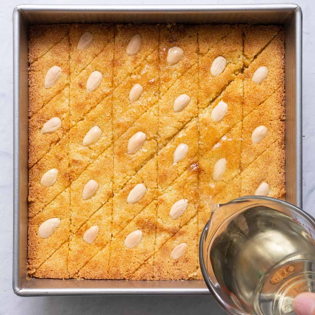 Pouring simple syrup over the namoura as soon as it comes out of oven.