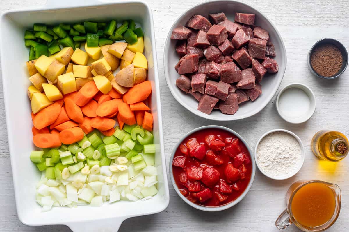 Ingredients for recipe: baking dish with chopped veggies, stew meat, diced tomatoes, seasonings, olive oil, broth, and flour.