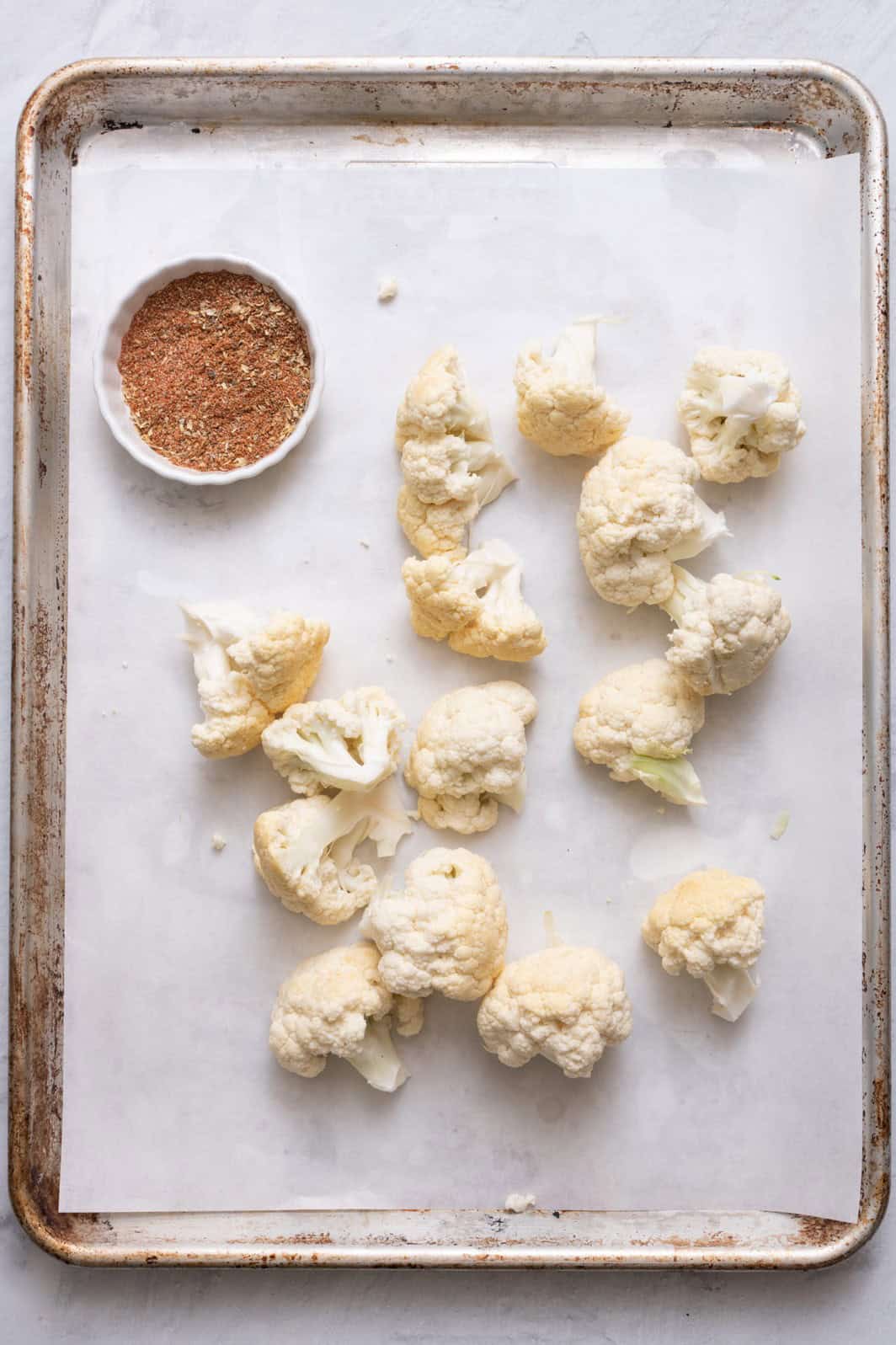 Cauliflower on a lined baking sheet with a bowl of seasoning nearby.