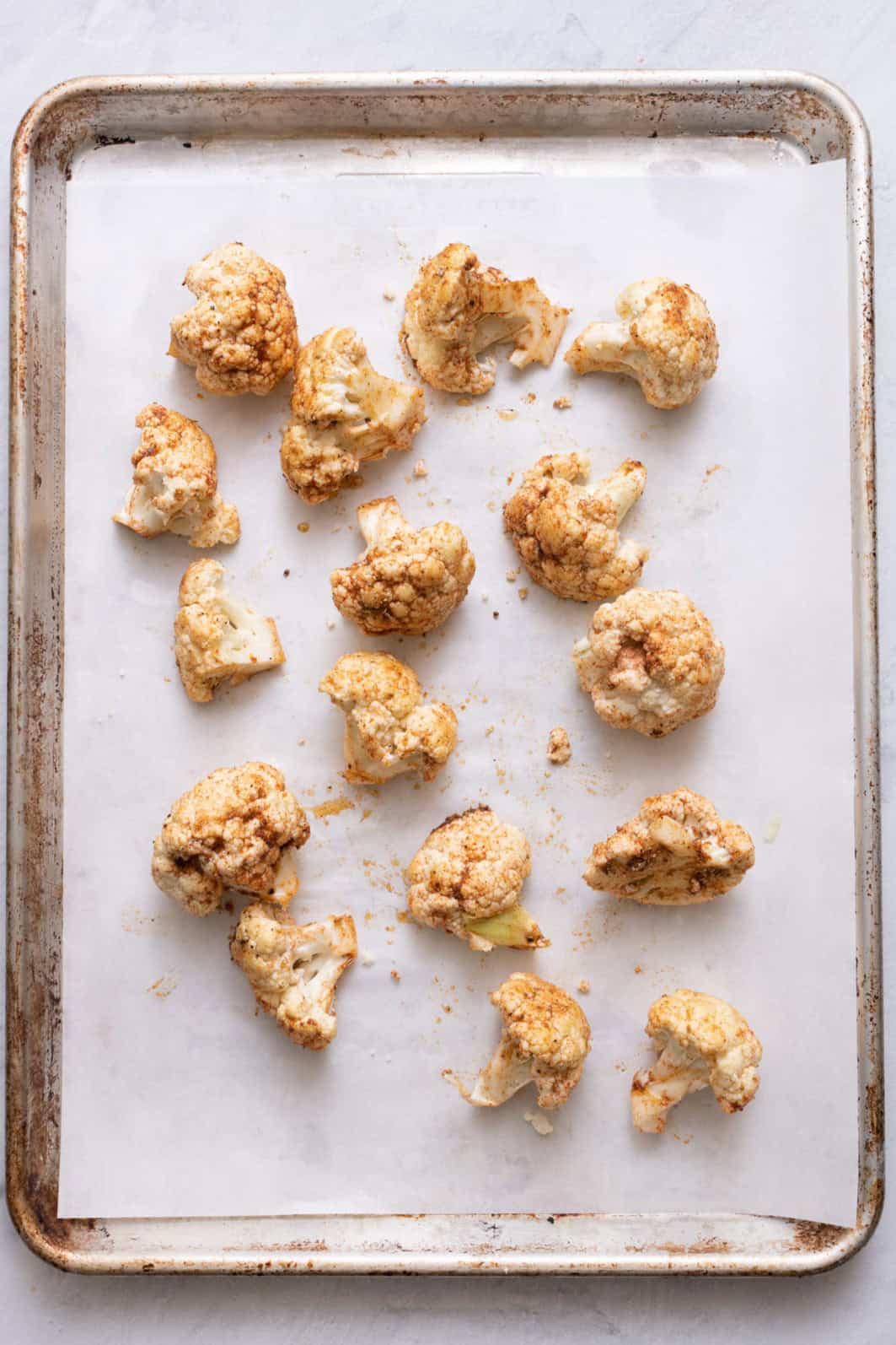 Seasoned cauliflower on a lined baking sheet.
