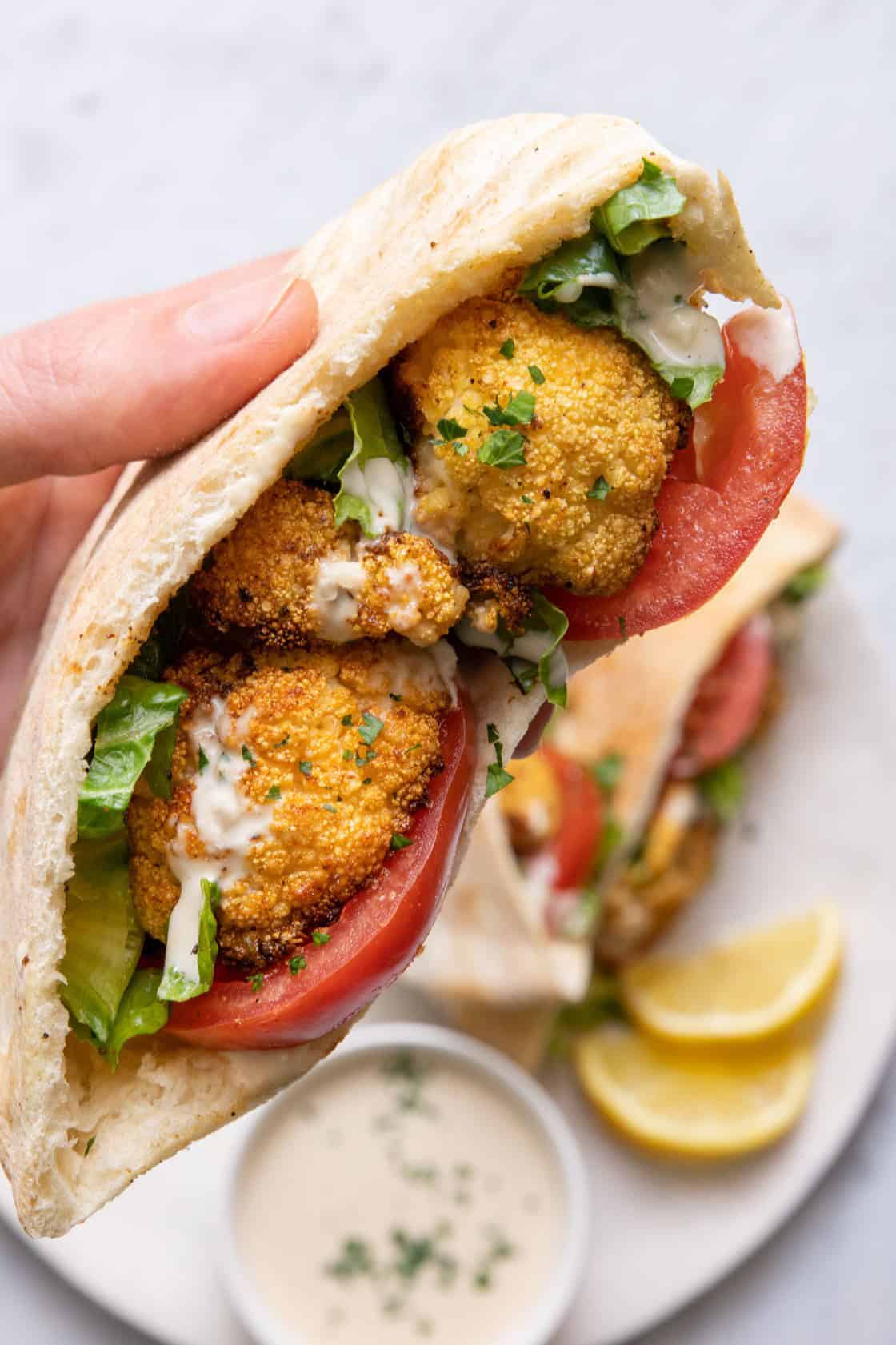 A hand holding one cauliflower pita, with more in the background.