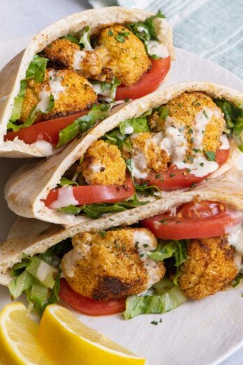 Three cauliflower pitas on a dish resting on top of one another with a small dish of tahini nearby.