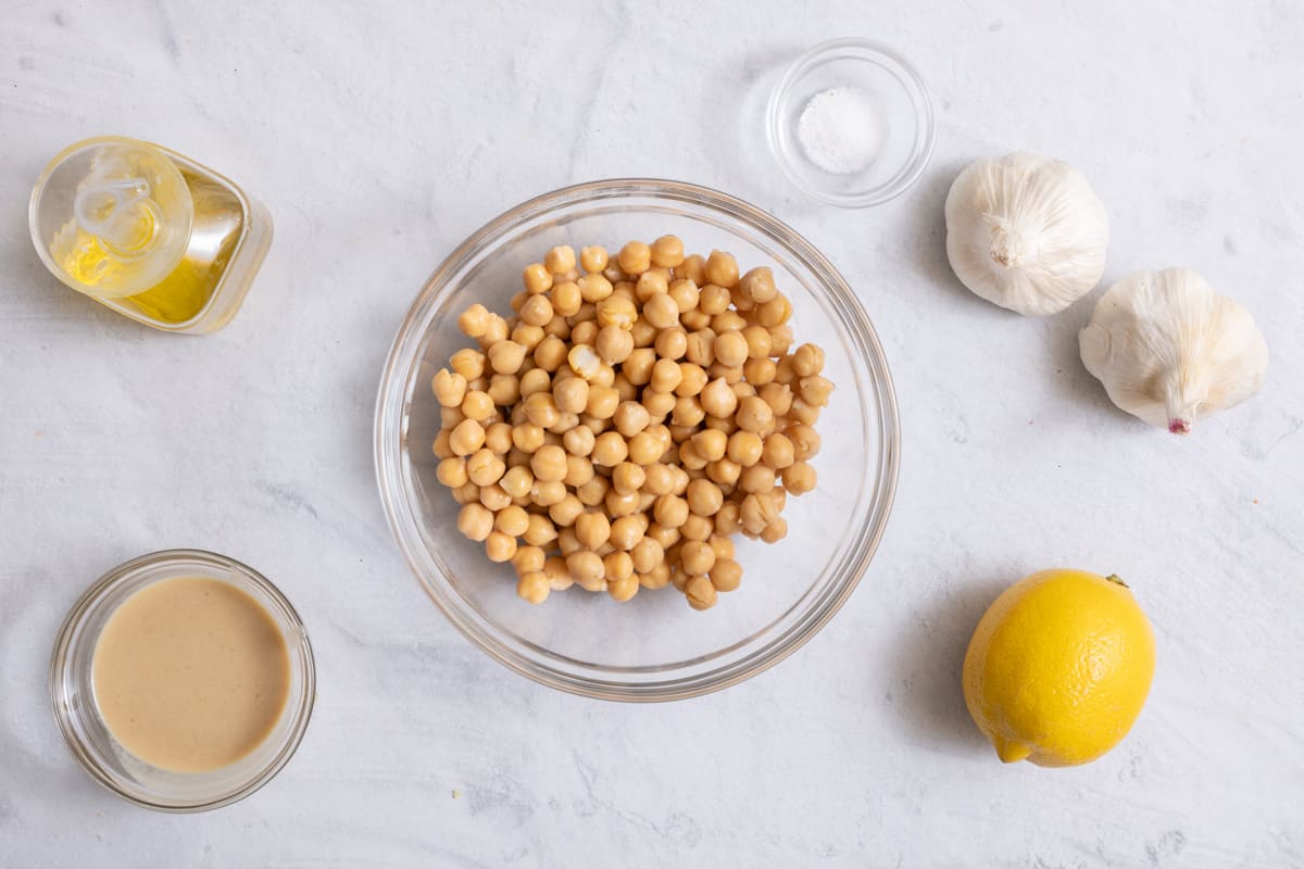 Ingredients for recipe: olive oil, tahini, chickpeas, salt, two heads of garlic, and a lemon.