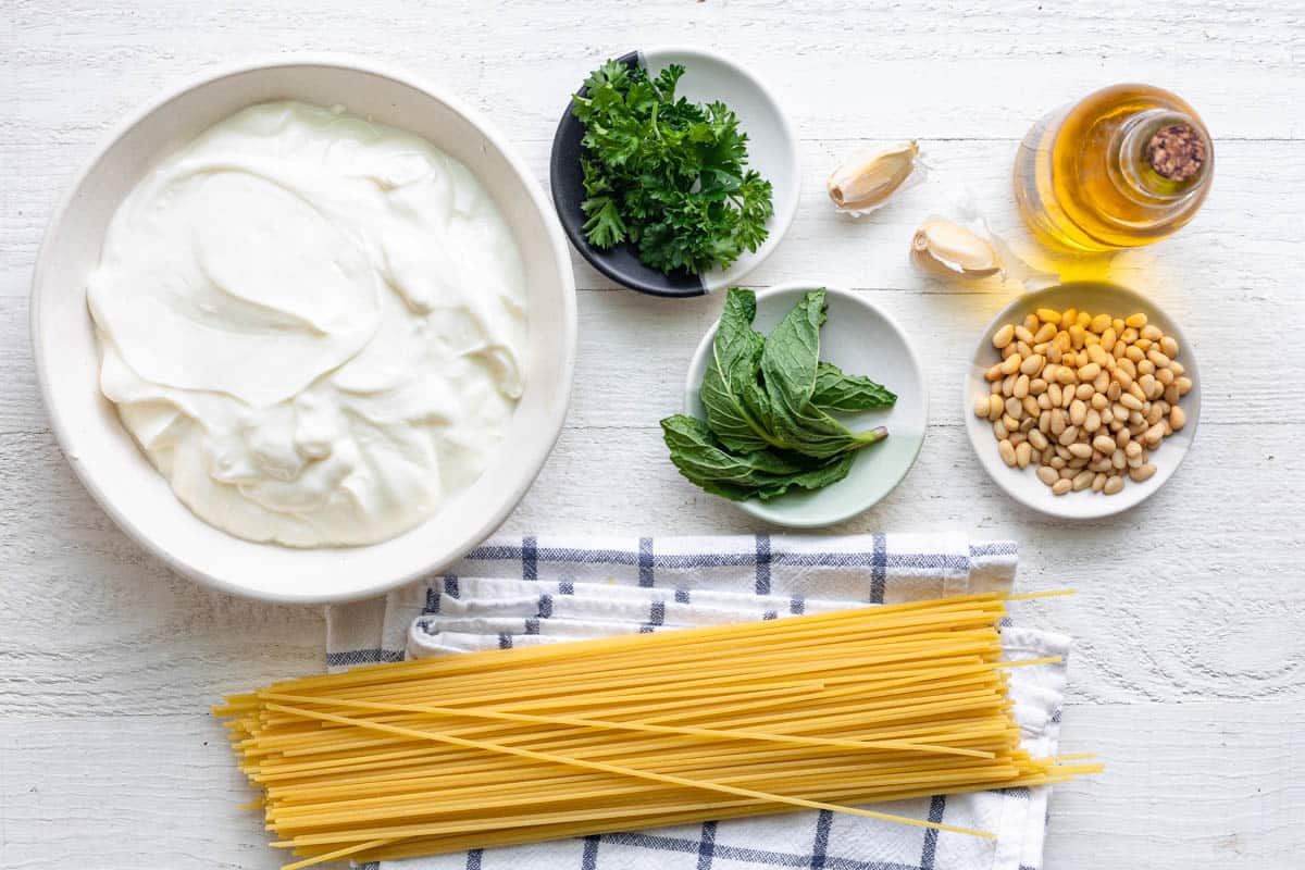 Ingredients for recipe: yogurt, dry spaghetti noodles, pine nuts, fresh parsley and mint, garlic cloves, and olive oil.