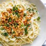 Spaghetti in Yogurt Sauce topped with pine nuts and chopped herbs, served in large white bowl.