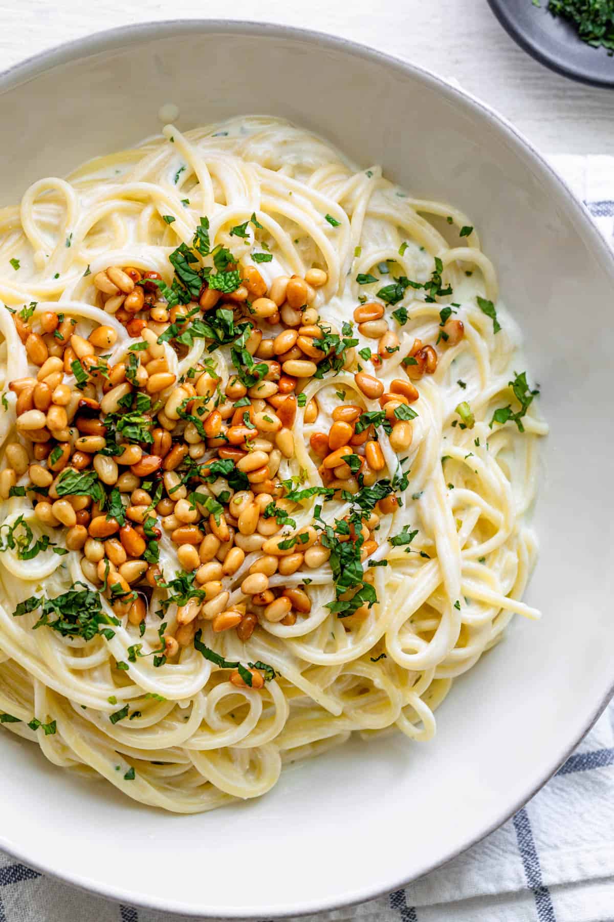 Spaghetti in Yogurt Sauce topped with pine nuts and chopped herbs, served in large white bowl.
