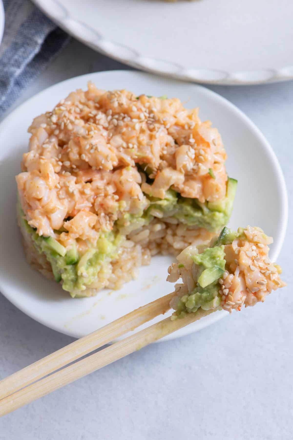 Chopsticks taking bite out of sushi stack made with shrimp.