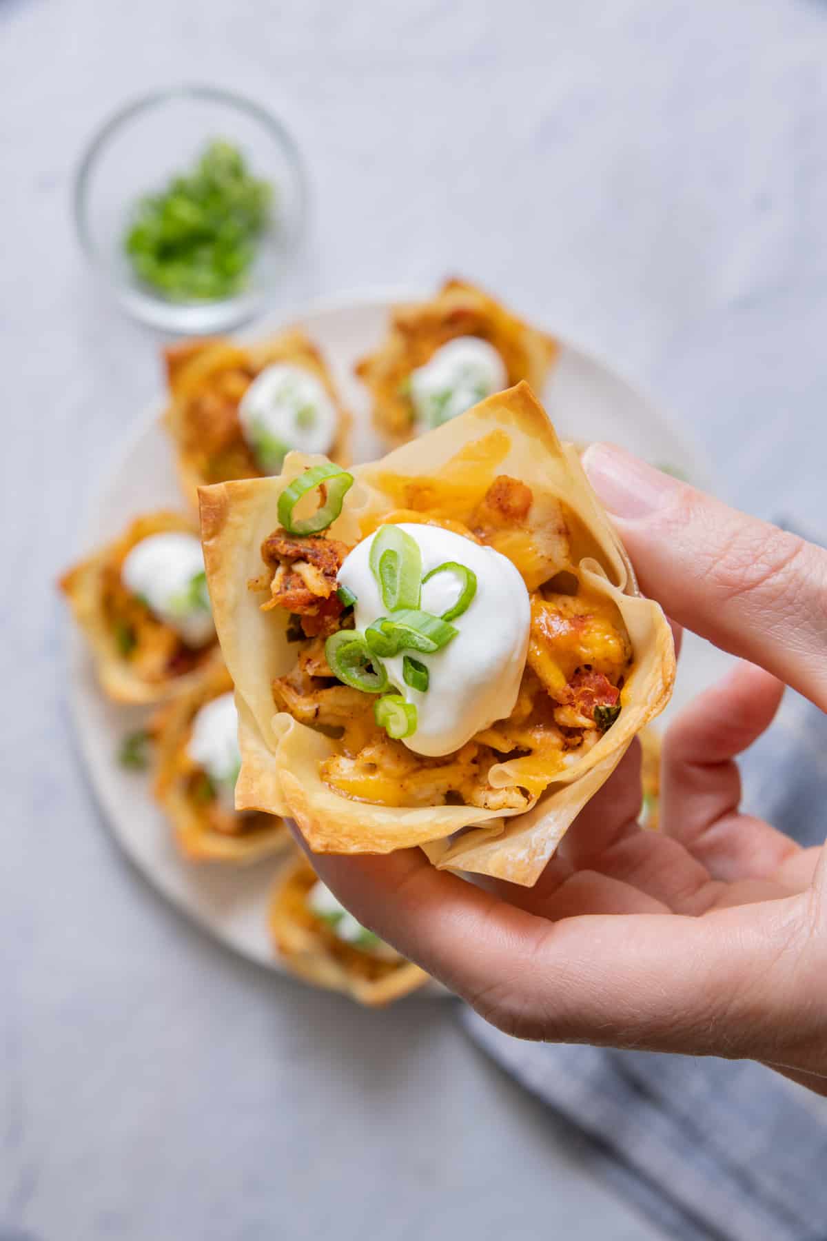 Hand holding a taco cup close up with sour cream and green onions.